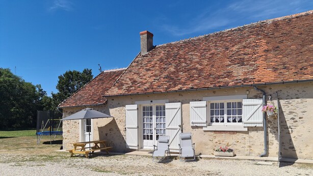 A stone building with a tiled roof, white shutters, a picnic table, and a swing set.
