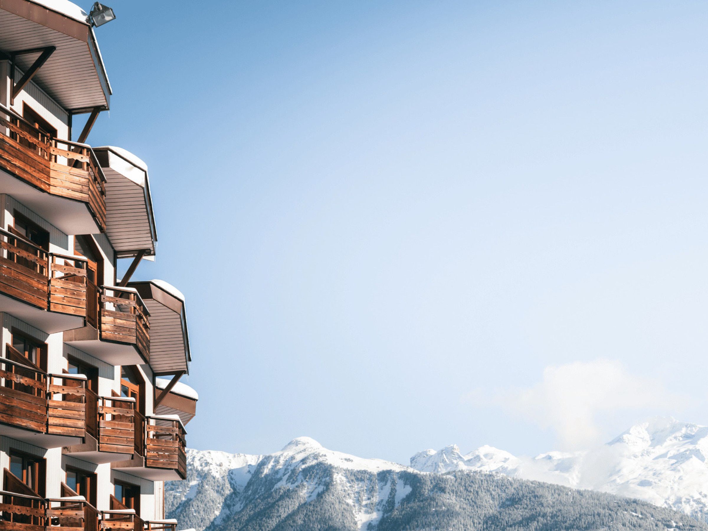 Un edificio de varios pisos con balcones, con montañas nevadas al fondo.