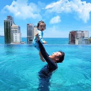 A man holding a child above water in a pool with a cityscape in the background. - Golden Lotus Grand (Da Nang)