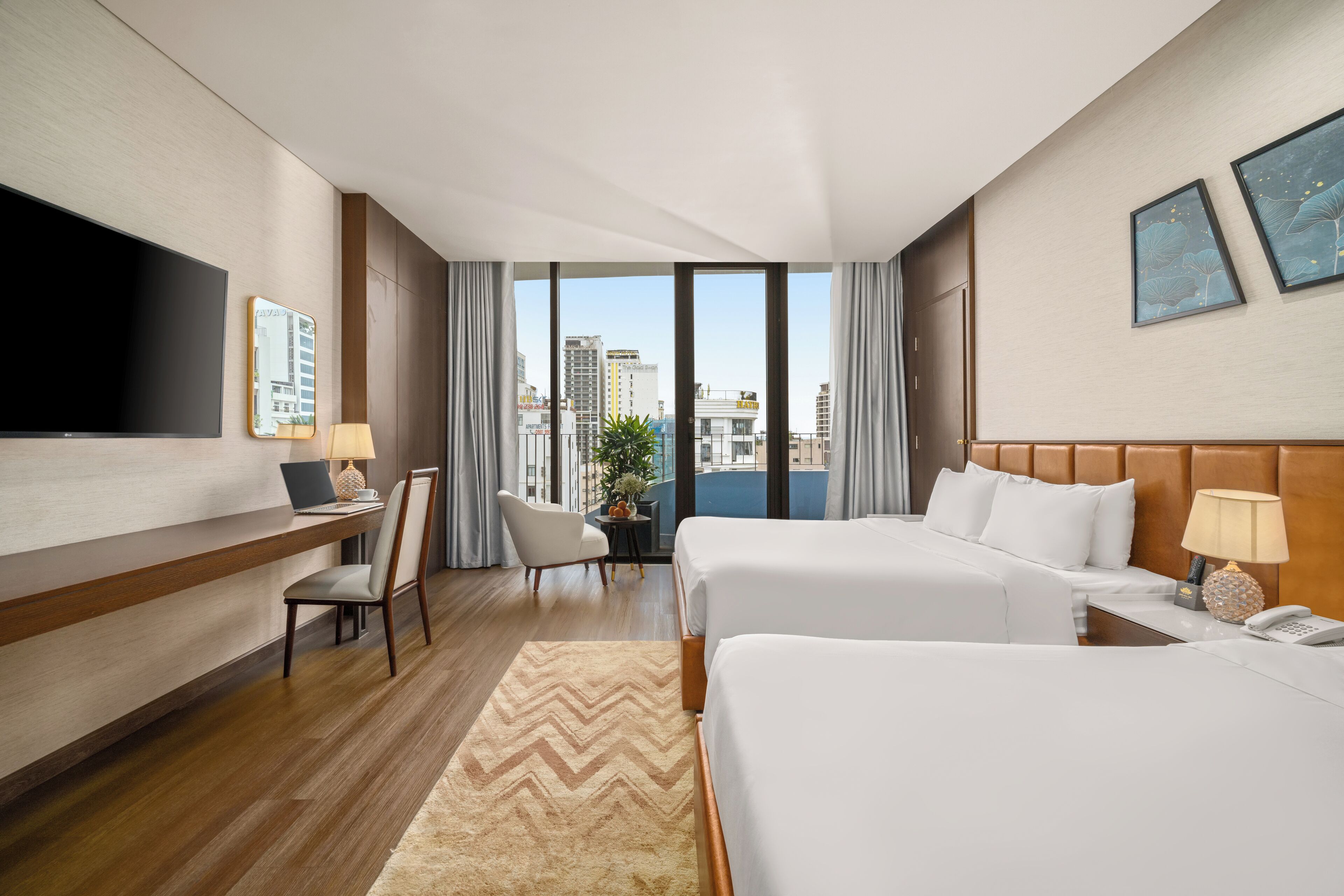 A hotel room with two beds, a desk with a laptop, a TV, and a view of the city.