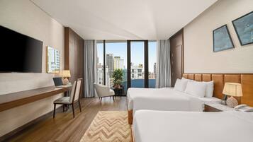 A hotel room with two beds, a desk with a laptop, a TV, and a view of the city.