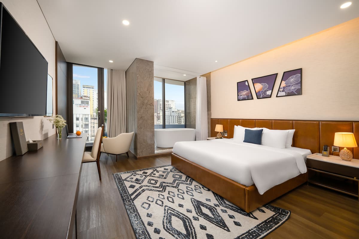 A modern hotel room with a large bed, a desk, a chair, and a view of the city.