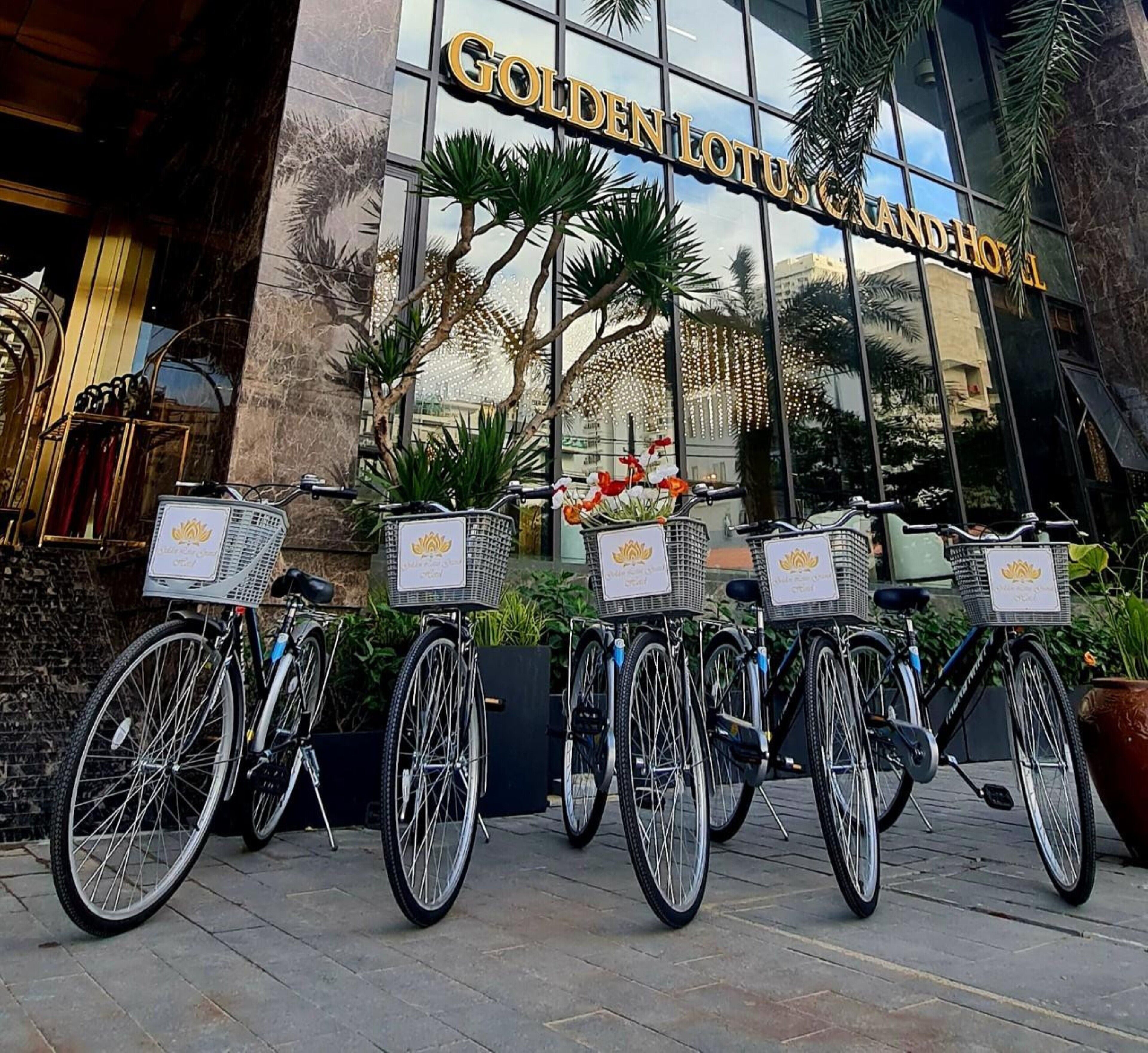 A row of bicycles parked in front of the Golden Lotus Grand Hotel, with baskets attached to the front.