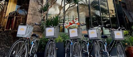A row of bicycles parked in front of the Golden Lotus Grand Hotel, with baskets attached to the front.