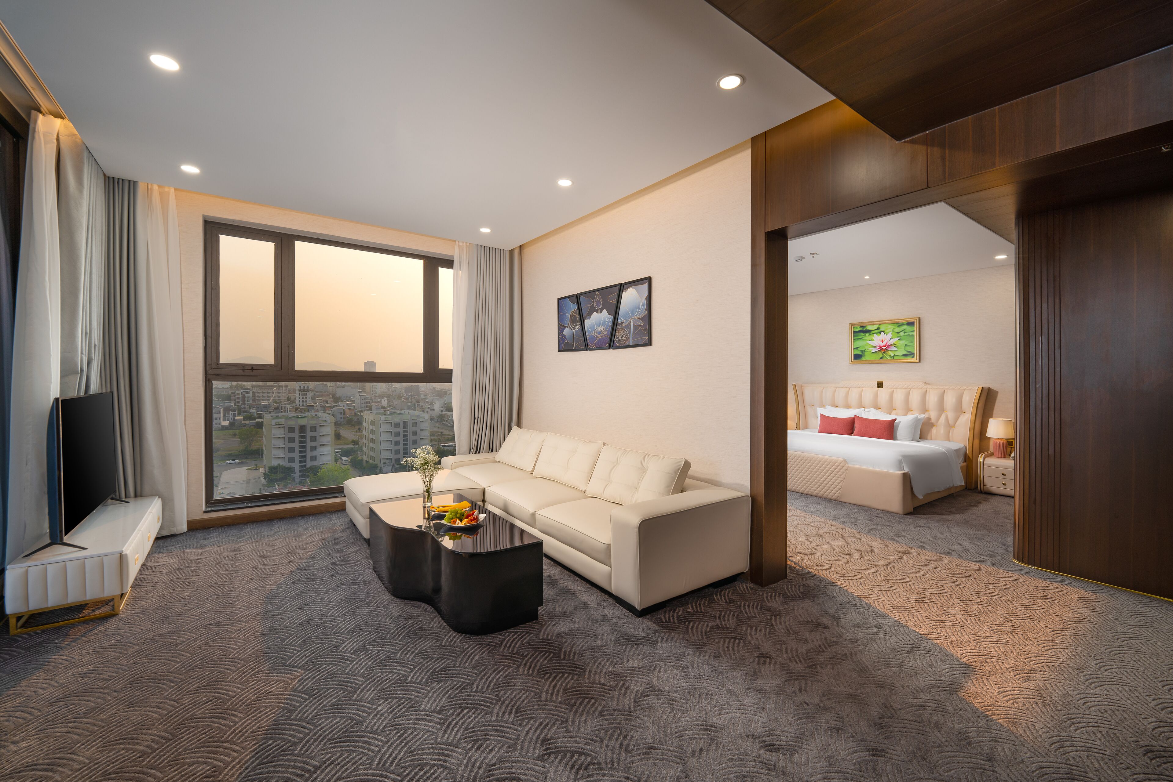 A modern hotel room with a large window, a sofa, a coffee table, and a bed.