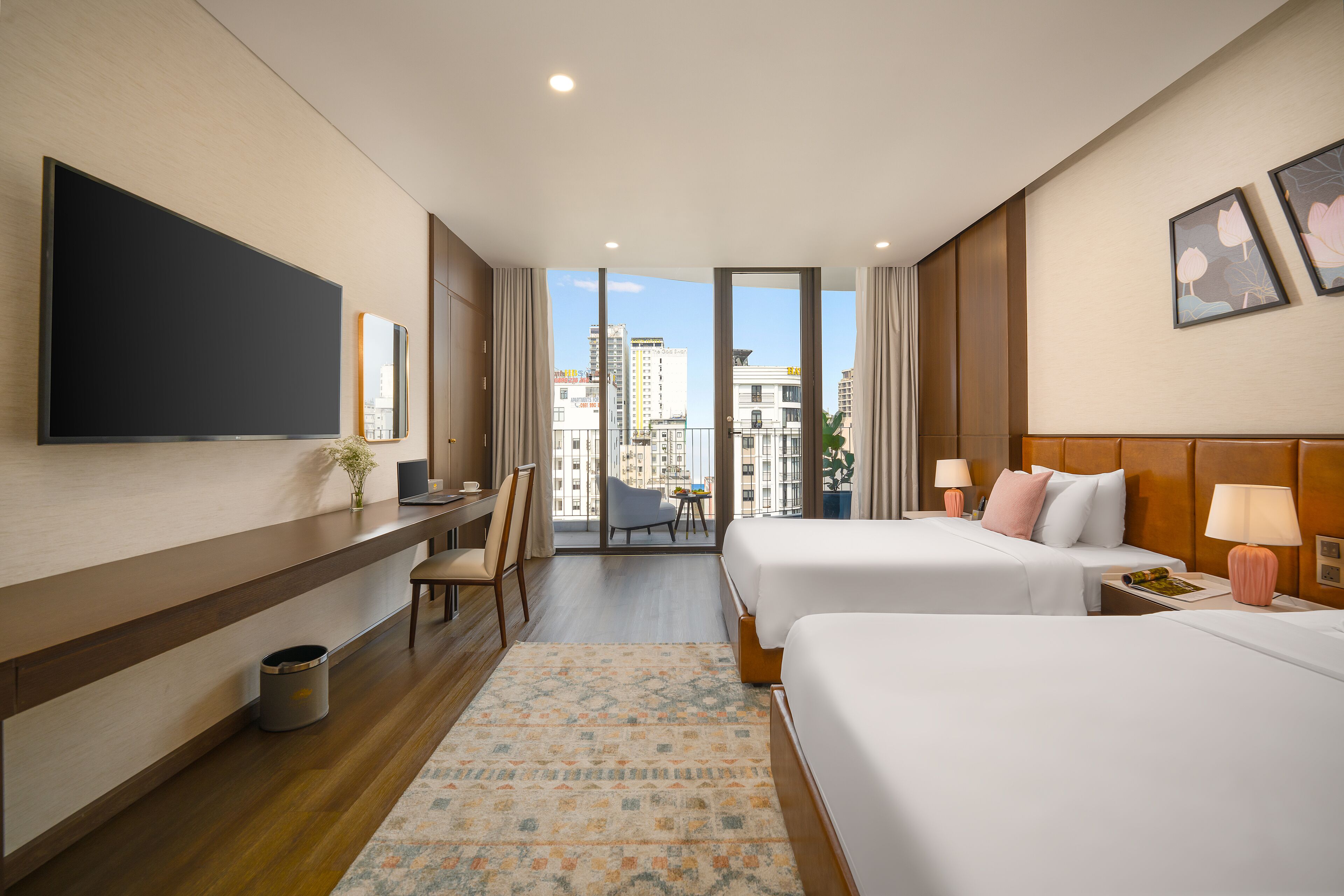 Habitación de hotel con dos camas, un escritorio, televisión y balcón con vistas a la ciudad.