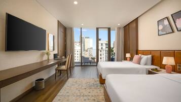 Habitación de hotel con dos camas, un escritorio, televisión y balcón con vistas a la ciudad.