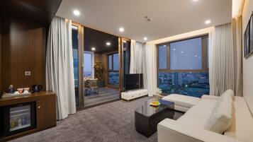 Una habitación de hotel moderna con sofá, televisor y zona de comedor con mesa y sillas.