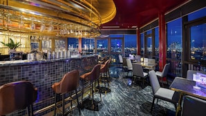 Eine Bar mit Blick auf die Stadt, Barhocker und einer hohen Decke.