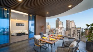 A modern dining area with a city view, featuring a wooden table set for four, surrounded by wicker chairs. - Golden Lotus Grand (Da Nang)