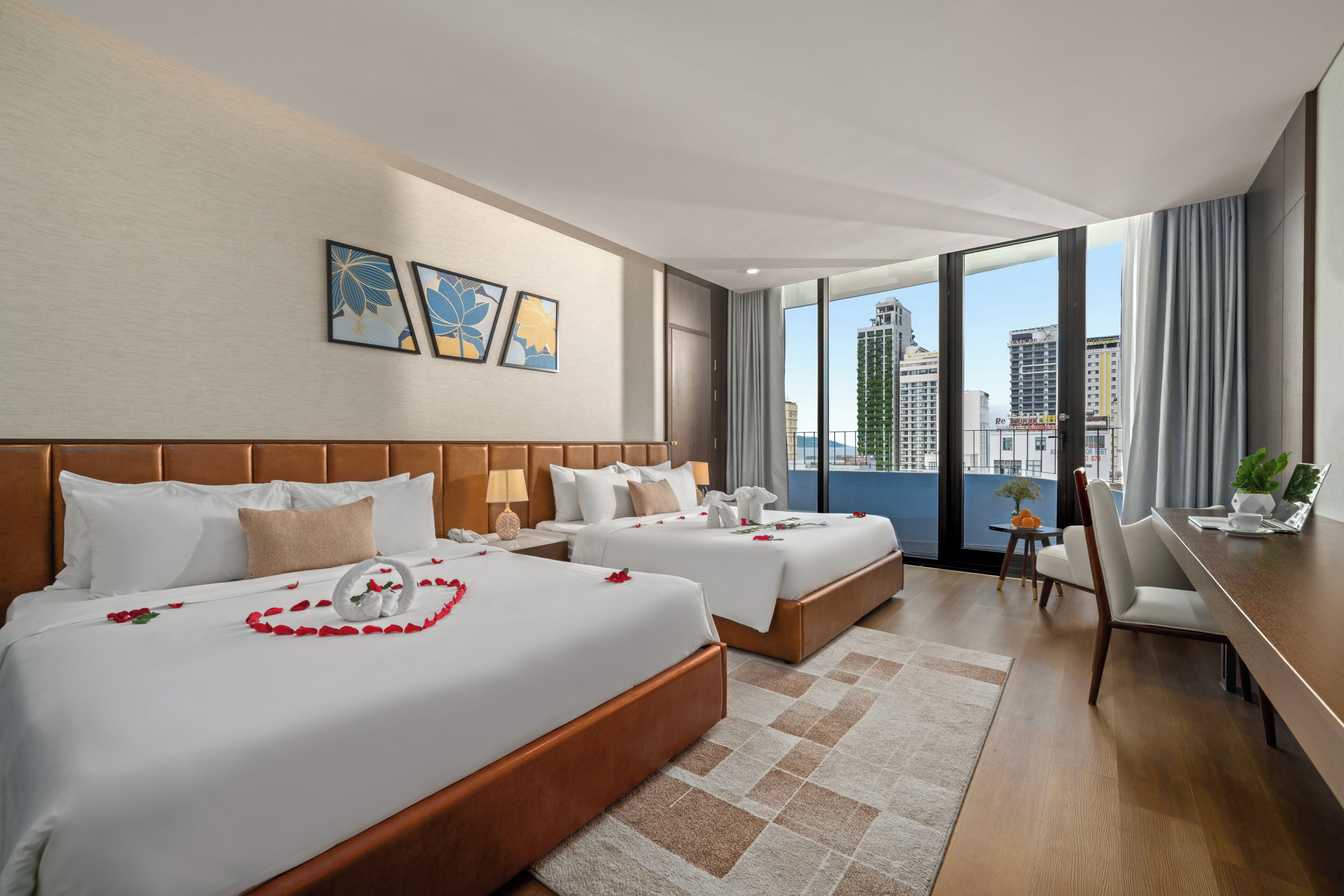 A hotel room with two beds, a desk, and a view of the city.