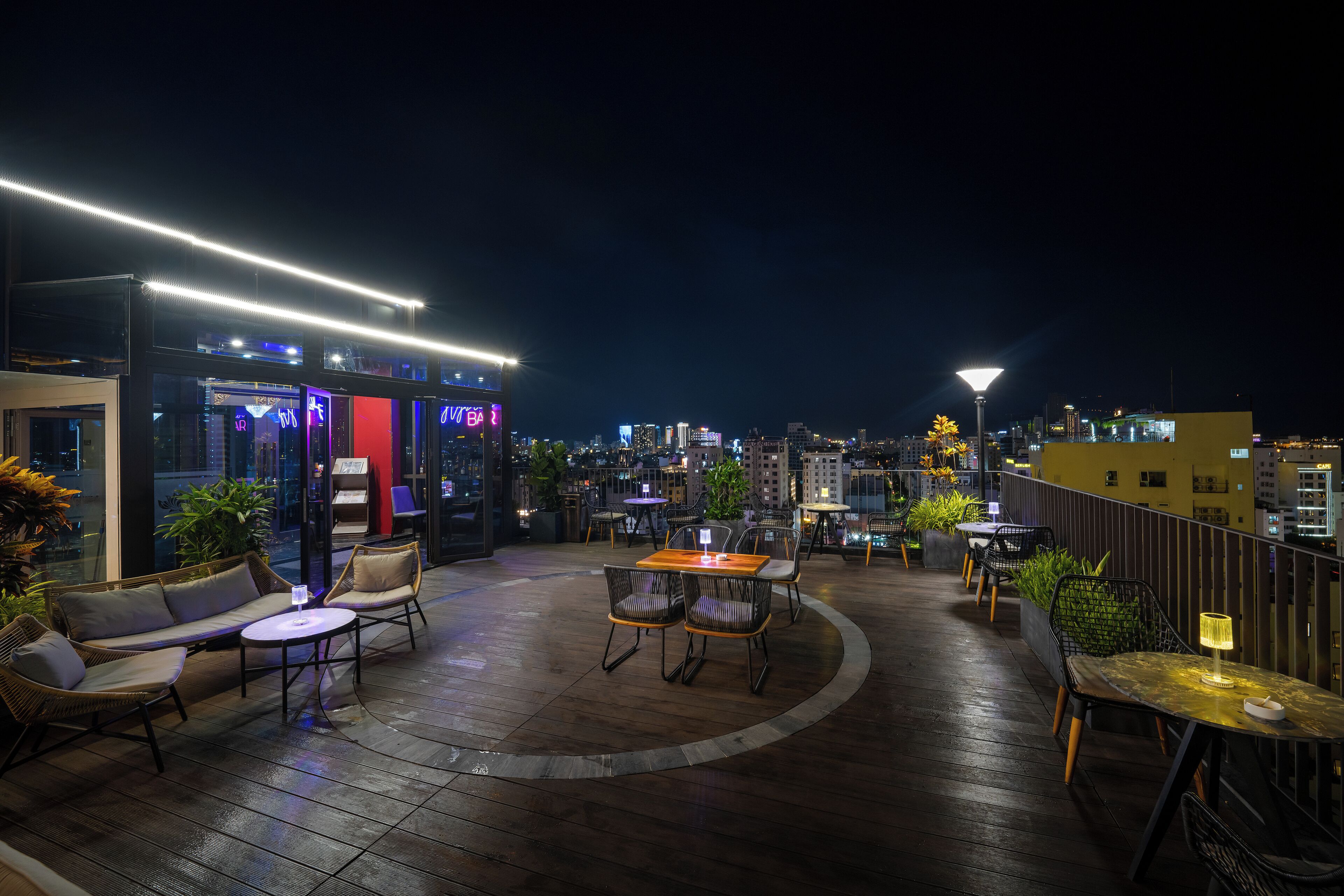 An outdoor patio area with seating and tables, surrounded by city views at night.