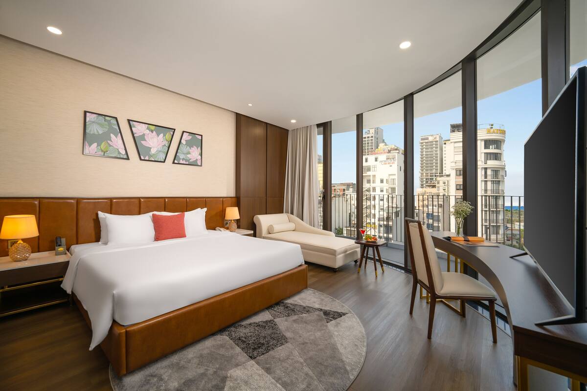 A modern hotel room with a large bed, a sofa, a desk, and a view of the city.