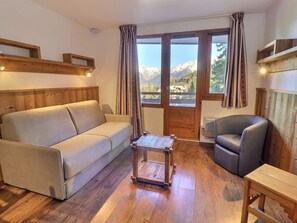 A cozy living room with a sofa, armchair, wooden coffee table, and a view of mountains through large windows.
