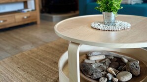 A round wooden table with a small potted plant on top, a woven placemat, and a bowl of decorative stones.