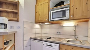 A compact kitchen with wooden cabinets, a microwave, a dishwasher, and a coffee maker. - Comfortable 2-Room + Alcove Apartment, Ski-in/Ski-out (La Tania)