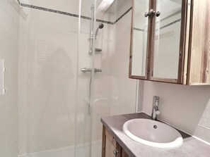 A bathroom with a glass shower enclosure, a sink with a mirror above it, and wooden cabinets. - Comfortable 2-Room + Alcove Apartment, Ski-in/Ski-out (La Tania)