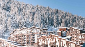 A snow-covered mountain resort with multi-story buildings featuring balconies and ski slopes in the background. - Cozy 2-room ski-in/ski-out, near shops (La Tania)