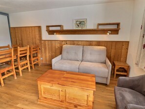 A living room with a sofa, wooden chairs, a coffee table, and a wooden shelf with a picture. - Comfortable 2-room apartment, ski-in/ski-out, near shops (La Tania)