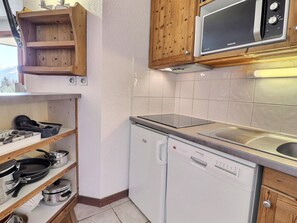 A compact kitchen with a microwave, dishwasher, and wooden shelves with cookware. - Comfortable 2-room apartment, ski-in/ski-out, near shops (La Tania)