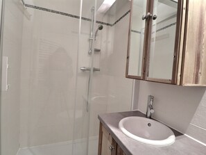 A bathroom with a glass shower enclosure, a sink with a mirror above it, and wooden cabinets. - Comfortable 2-room apartment, ski-in/ski-out, near shops (La Tania)