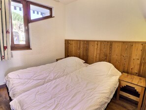 A room with a wooden headboard, two beds, a wooden nightstand, and a window with curtains. - Comfortable 2-room apartment, ski-in/ski-out, near shops (La Tania)