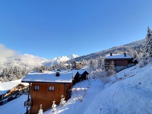 Een houten chalet met balkon, omgeven door met sneeuw bedekte bomen en bergen op de achtergrond.