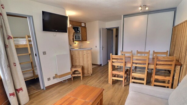 A compact living space with a wooden table, a sofa, a TV, a kitchenette, and a wooden cabinet. - Comfortable 2-room apartment, ski-in/ski-out, near shops (La Tania)