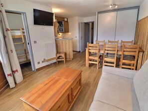 Um espaço compacto com mesa de madeira, sofá, televisão, pequeno espaço de cozinha e armário de madeira.