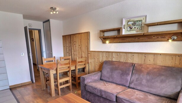 A cozy room with a wooden dining table, chairs, a sofa, and a wooden cabinet.