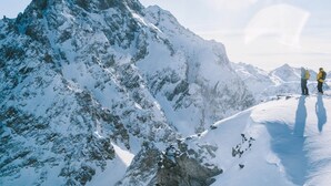 A snow-covered mountain peak with two hikers in the distance.