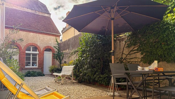 Eine Terrassenfläche mit Tisch, Stühlen, einem gelben Liegestuhl, einem Sonnenschirm und einer weißen Bank.