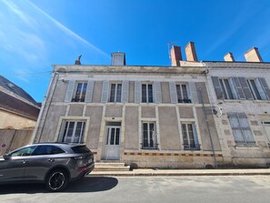 A two-story building with a flat roof, multiple windows with shutters, and a car parked in front.