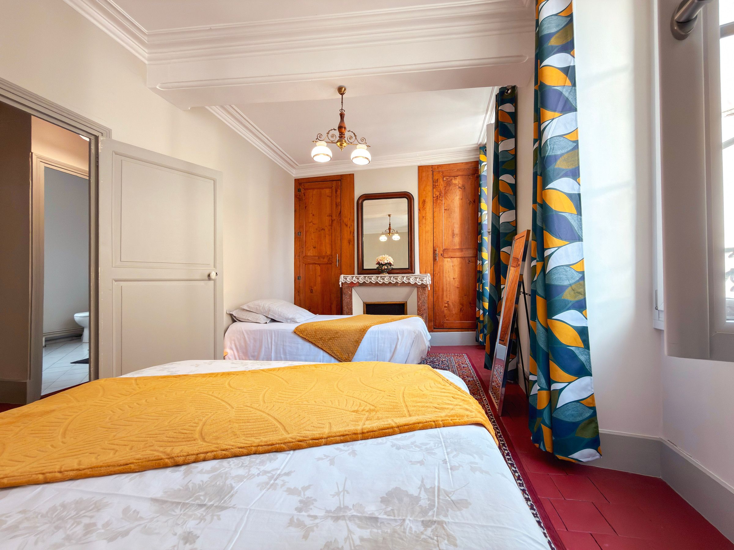 Een slaapkamer met twee bedden, een houten garderobe, een spiegel en een raam met gordijnen.