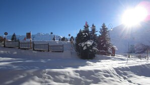 En snötäckt skidbacke med ett trästaket, en liten byggnad och en klarblå himmel.