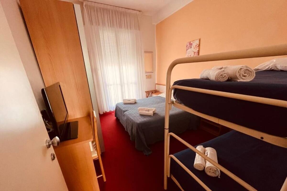 A hotel room with bunk beds, a desk with a computer, a chair, and a window with curtains.