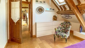 A room with a wooden ceiling, a white dresser, a floral armchair, and a door leading to another room.