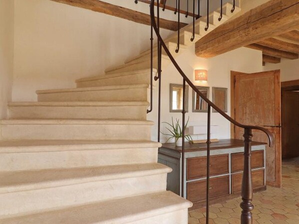 A staircase with wooden railings and beige steps leading to a landing area with a wooden cabinet and a potted plant.