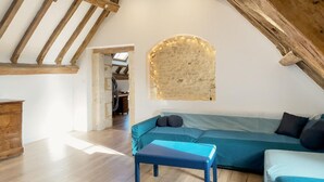 A loft-style room with exposed wooden beams, a stone wall with string lights, a blue sofa, and a wooden bench.