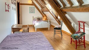A bedroom with a sloped ceiling, wooden beams, a bed, a chair, and a small table.