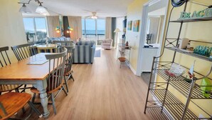 A hotel room with a dining area, a balcony with a view, and a shelf with items. - New Private Ashworth Resort Direct Oceanfront View (North Myrtle Beach)