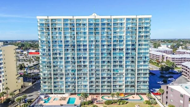 A high-rise hotel with a modern glass facade, multiple balconies, and a pool area with sun loungers. - New Private Ashworth Resort Direct Oceanfront View (North Myrtle Beach)