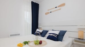 Una cama bien hecha con una bandeja de fruta y una botella, una mesita de noche con una lámpara, y dos paletas de madera en la pared.