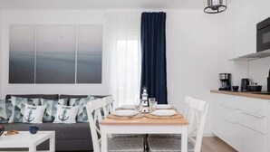 Una sala moderna con comedor, un sofá con cojines geométricos, una mesa de centro y vista al mar a través de una ventana con cortina oscura.