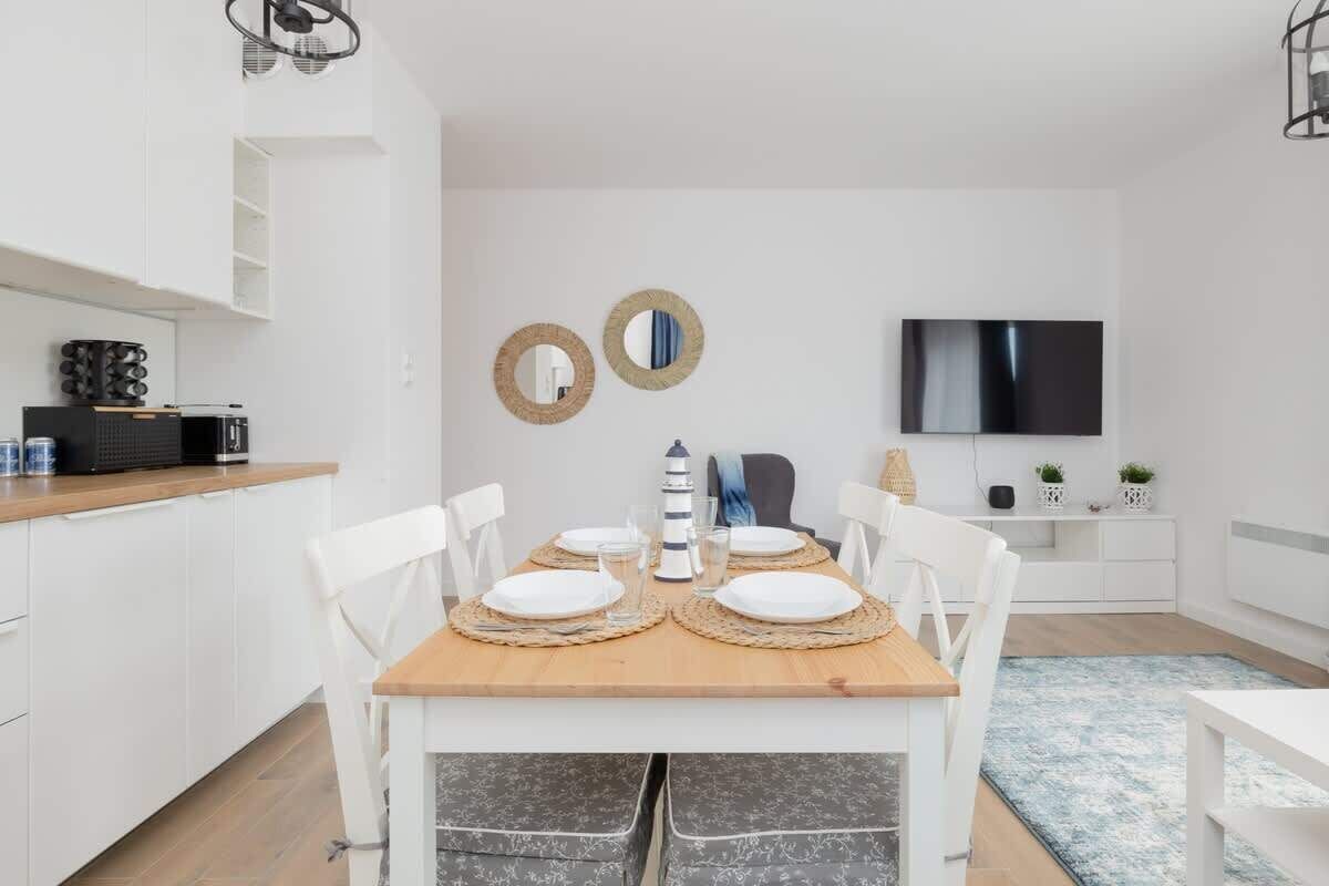 Een moderne keuken met witte kasten, een houten eettafel gedekt voor vier personen, en een televisie aan de muur.