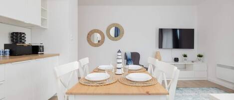 Een moderne keuken met witte kasten, een houten eettafel gedekt voor vier personen, en een televisie aan de muur.