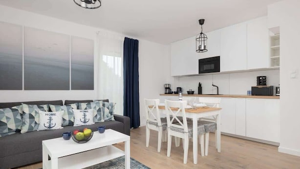 Una sala de estar moderna con un sofá gris, una mesa de centro blanca y un comedor con sillas blancas y una mesa de madera.