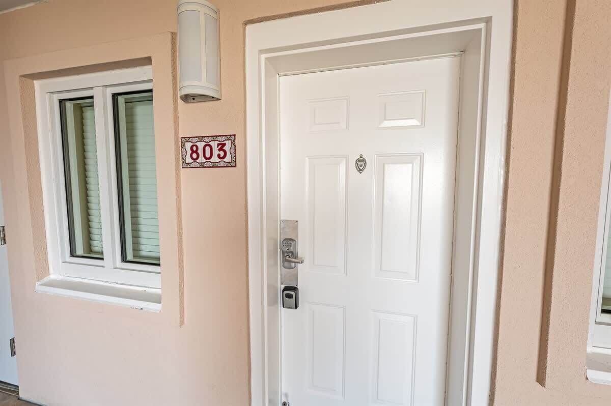 A white door with a keypad lock, a window with blinds, and a wall-mounted sign with the number 803.