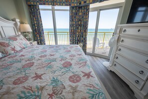 Relax in this serene beachfront room with a large bed, dresser, and TV, plus a balcony with ocean views.