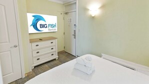 Ein Hotelzimmer mit einem Bett, einem Schminktisch, einem Spiegel und einem an der Wand befestigten Fernseher, der das Logo von Big Fish Rentals zeigt.